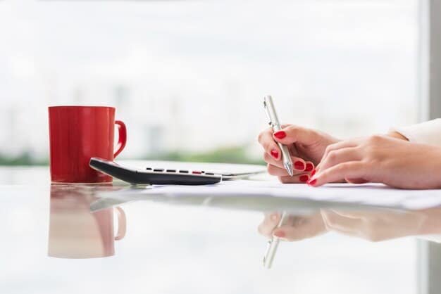 A close-up shot of a hand holding a pen over a tax form, with financial documents and a calculator in the background, emphasizing the complexity of tax preparation.