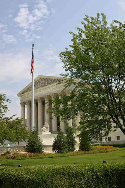 The Supreme Court building in Washington D.C., focusing on the American flag waving in front. The image should be taken on a sunny day to enhance the sense of authority and clarity.