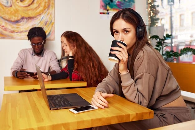 A student happily working on a laptop in a bustling cafe, showing the combination of independent work and social interaction that a gap year can offer.