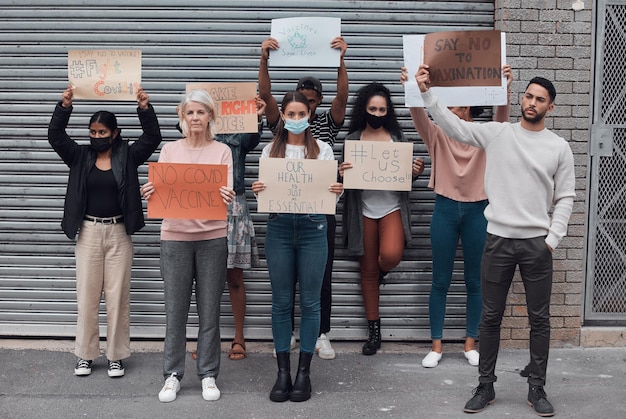 A medium shot of a diverse group of people protesting outside a government building, holding signs with messages about funding and government services. Some signs feature the text 
