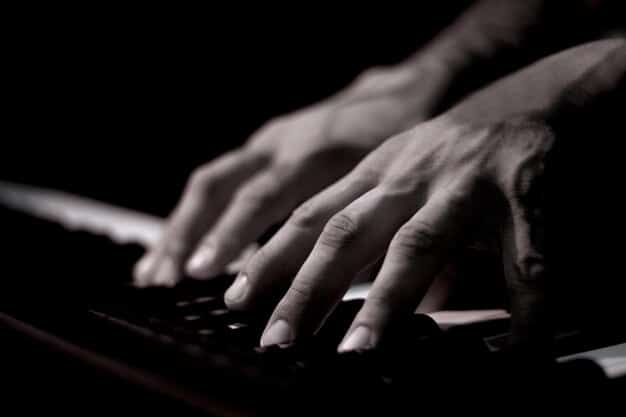 A dark, shadowy figure behind a computer screen, fingers typing rapidly on the keyboard. Lines of code are visible on the screen, hinting at a cyberattack in progress. The scene evokes a sense of urgency and highlights the threat posed by cybercriminals targeting critical infrastructure related to the National Security Alert: Increased Cyberattacks Targeting Critical Infrastructure.