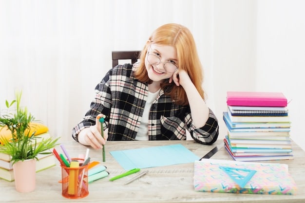 A student writing on a notebook and smiling with books, a laptop, and stationary scattered on her desk, which implies she is studiously working to maximize productivity through planning and proper resource manangement from the tips given by The Truth About Online Education: Debunking Myths and Maximizing Success and getting the study tips correct.