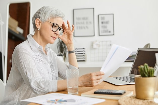 A senior woman looking stressed while reviewing bills at her kitchen table. A calculator and a stack of papers are visible, symbolizing financial strain.